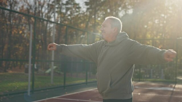An elderly man is exercising on an outdoor sports field. Fitness for pensioners