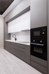 The facade of a modern kitchen set. Black kitchen mixer, hob, oven and microwave. Side view