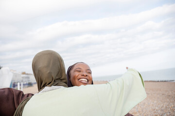Two Muslim women embracing on beach
