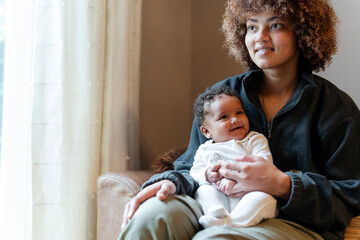 Young mother holding baby girl on lap at home © Cultura Creative