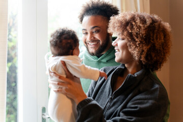 Smiling parents looking at baby daughter at home - obrazy, fototapety, plakaty