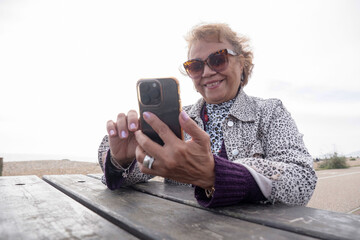 Senior woman using smart phone while sitting by picnic table on beach
