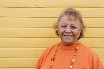 Portrait of smiling senior woman against yellow wall
