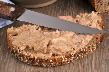 Tranche de pain aux graines avec des rillettes et un couteau en gros plan.