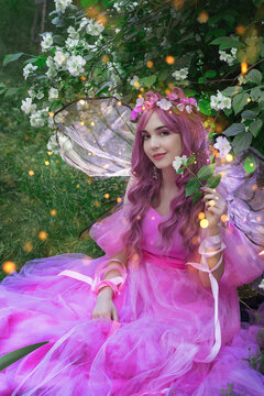 A beautiful young fantasy woman in the image of a flower fairy sits in a meadow of flowers, the wings of a butterfly shine magically. Fairy art girl.