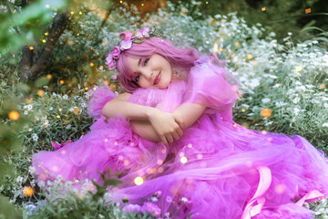 A beautiful young fantasy woman in the image of a flower fairy sits in a meadow of flowers, the...