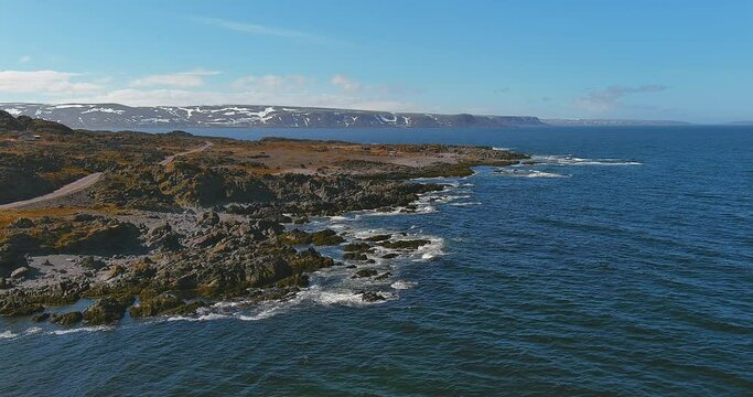 Aerial view of coastline along the road 8100 to Hamningberg  with waves crashing into rocky shore from Barents Sea in sunny summer weather, Varanger Peninsula, Norway.