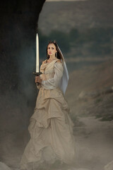 A beautiful red-haired girl in an old medieval dress with swords stands in the mountains and looks into the distance. Fairytale story about a princess. magic light. Warm artistic work. © olenakucher