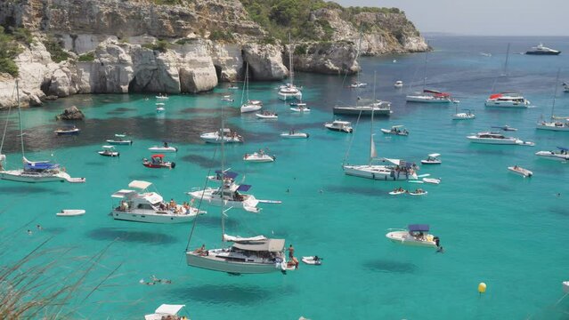 White yachts floating on turquoise shallow water of Cala Macarella in Menorca Island Spain, idyllic summer vacation travel destination in Mediterranean Sea
