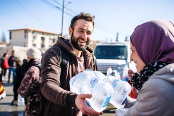 A male volunteer distributes boxes of clean drinking water and humanitarian aid to a war-affected woman in a hijab, civilians affected by the war conflict