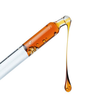 Drop of a yellow oily liquid dripping from a pipette close up on a white background