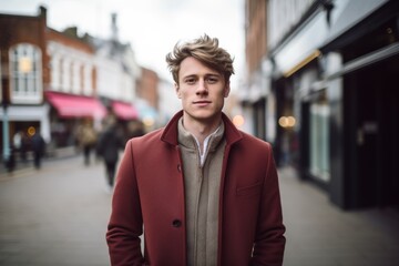 Portrait of a handsome young man with blond hair in a red coat on a city street.