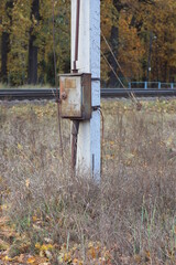 one gray closed metal box with electrical wires on a white concrete pole in dry grass on the street