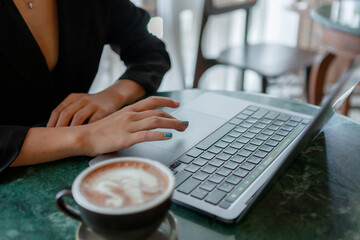  A woman works and types on a laptop keyboard with a coffee cup on the table.