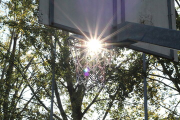 Compositional shot of the sun, with ray effect inside the basketball hoop.