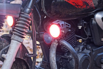 one small round red glass headlight turn signal on a black motorcycle on the street - obrazy, fototapety, plakaty