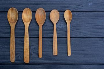 a set of five old brown wooden spoons lie on a black table