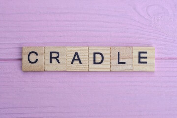 word cradle from small gray wooden letters lies on a pink wooden table