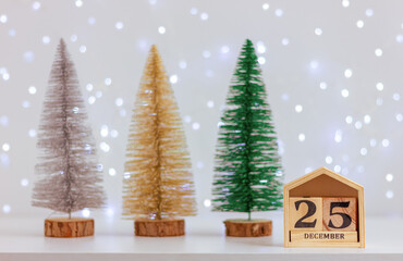 small Christmas trees and wooden calendar with December 25 and festive light. celebration, decorations, winter holiday