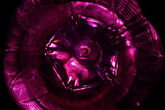 C&iacute;rculo de la base pl&aacute;stica de un envase para contener l&iacute;quidos con luz magenta forma anillos conc&eacute;ntricos luminosos formando un original dise&ntilde;o abstracto con fondo negro
