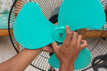 A man removes the plastic fan blade lock nut of an oscillating electric fan. Cleaning and repairing...