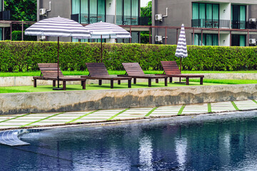 Brown wooden relaxing chairs with big umbrellas beside swimming pool.  View of beach chairs placed...