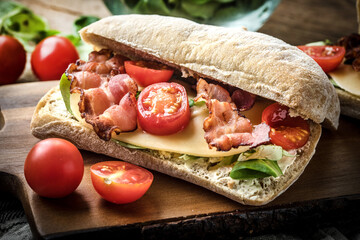 Ciabatta sandwich with arugula salad, bacon and yellow cheese.