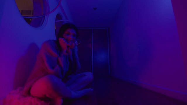 Young mad woman rocking back and forth while sitting on the floor and having a panic attack in a room with flashing neon light. Zoom Shot