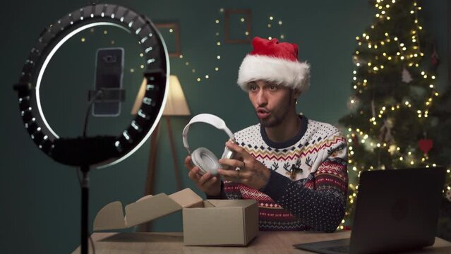 Good looking Arabic man unboxing a new wireless headphones and reviewing a few electronic products on camera in Christmas Eve