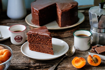 Chocolate cake with chocolate icing with apricot jam and cream inside. wooden background, side view