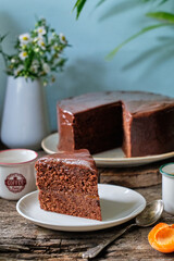 Chocolate cake with chocolate icing with apricot jam and cream inside. wooden background, side view