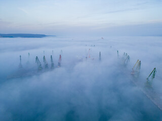 Aerial view of port cranes protruding through the morning fog