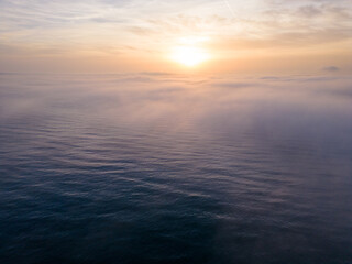 Obraz premium Aerial view of a sunrise sea with a blanket of morning fog and morning sunbeams shining through