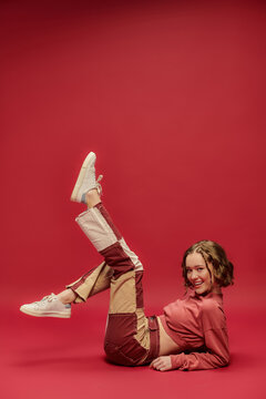 self-expression, full of joy girl in patchwork pants and cropped long sleeve sitting on red backdrop