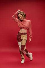 happy stylish and young woman in patchwork pants and cropped long sleeve posing on red backdrop