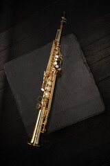 Straight Soprano Golden Saxophone on a black cube on a black floor of concert stage. Shallow depth...