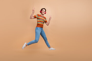 Fototapeta na wymiar Full length portrait of energetic excited person jump show v-sign listen music headphones empty space isolated on beige color background