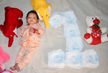 One month old baby girl photoshoot, one letter is written with diaper, baby is looking at camera ,...