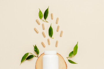 Supplement white bottle with herbal pills and green leaves close up on wooden podium, top view. Medical bottle mockup, organic medication. Natural herbal vitamins, healthy lifestyle.
