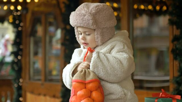 Little warmly dressed girl is holding a bag of tangerines. At the Christmas market.