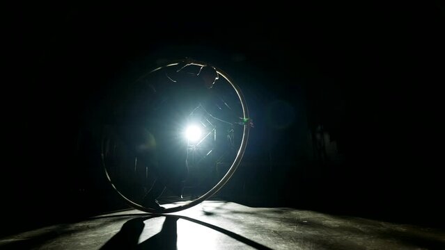 enigmatic acrobatic trick with hoop, man spinning in big hoop, silhouette in contour light