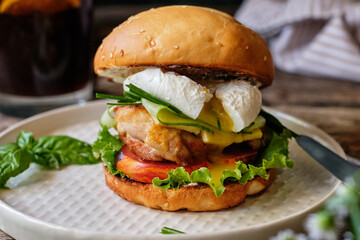 Homemade burger with cheese, lettuce, cucumber, tomato, chicken, poached egg. Wooden background, side view.
