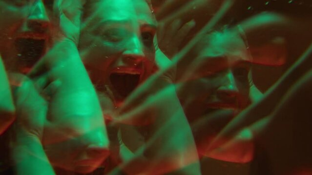Frightened woman holding head in hands and screaming in front of the mirror, having a panic attack or emotional breakdown in bathroom with neon light. Kaleidoscope effect, mental disorder concept
