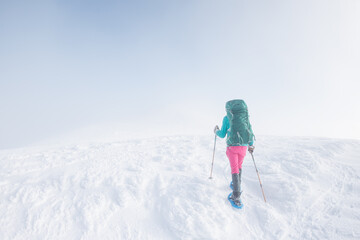 Fototapeta na wymiar Climber in the mountains. A girl with a backpack and snowshoes walks through the snow.