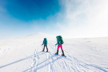 Fototapeta na wymiar winter activity. Two women walking in snowshoes in the snow, winter hiking, two people in the mountains in winter.
