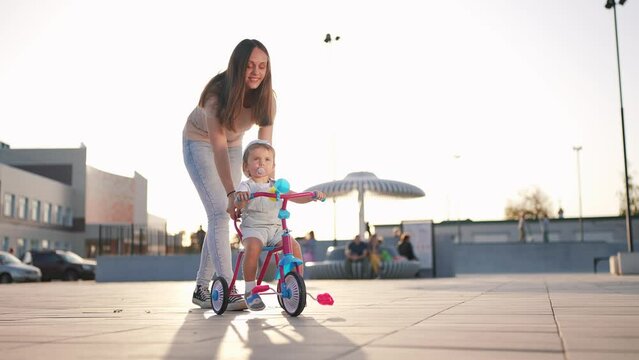 mother teaches son baby to ride a children bike. happy family kid dream concept. child baby rides a bike dad helps. mother day concept lifestyle. child playing riding a bike outdoors