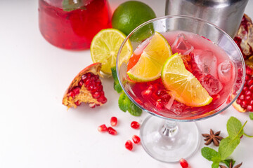 Pomegranate martini cocktail, iced cool boozy drink with fresh pomegranate juice, whiskey and lime slices, white background copy space - obrazy, fototapety, plakaty