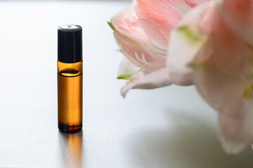 Dark glass rollerball bottle with natural aroma oil  on background with flowers, aromatherapy with...