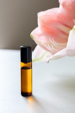 Dark glass rollerball bottle with natural aroma oil  on background with flowers, aromatherapy with essential oils.