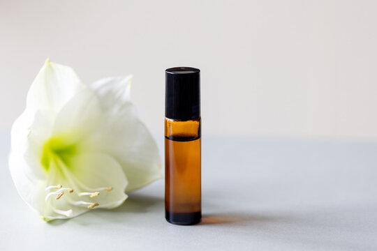 Dark glass rollerball bottle with natural aroma oil  on background with flowers, aromatherapy with essential oils.